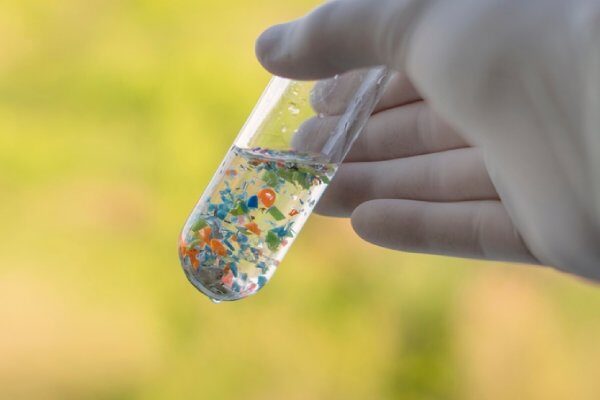 mano di scienziato con provetta contenente acqua piena di microplastiche